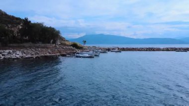Yunanistan 'da, ahşap balıkçı tekneleri ve küçük geleneksel tekneler doğal bir körfezdeki eski bir ahşap rıhtıma demirliyorlar. Kayalık sahil ve günbatımı manzarayı tamamlıyor..
