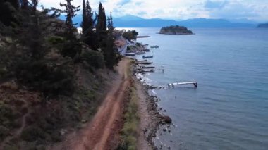 Bir Yunan adasındaki bu kıyı yolu sessiz mavi suların yakınından geçer ve ahşap balıkçı limanlarından geçer. Selvi ve diğer ağaçlar kıyı şeridi boyunca doğal gölgeler sağlar..