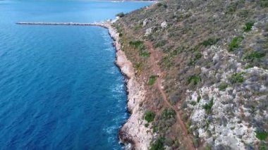 Bir Yunan adasında doğal bir koy bir dalgakıranla korunur. Dar kayalık bir patika yukarıdaki yamaca tırmanıyor ve geniş Akdeniz manzarası sunuyor..