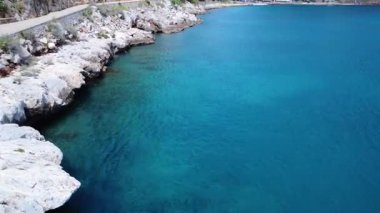 Yunanistan 'da yaz kayalıkları, tenha bir Akdeniz plajına ulaşmak için dağa oyulmuş gizli kayalık bir patikayla mavi denize dökülüyor..