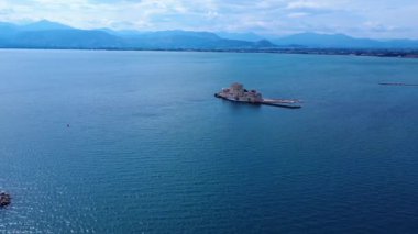 Yunanistan 'ın güneyindeki tarihi Nafplio limanı, sakin Akdeniz suları ve görünür bir deniz kalesiyle yukarıdan gösteriliyor. Taştan dalgakıranlar bu manzaralı limana koruma sağlar..