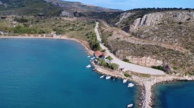 Bu yaz Yunanistan 'dan gelen insansız hava aracı görüntüleri, sakin Akdeniz sularına demirlemiş geleneksel ahşap balıkçı teknelerinin bulunduğu doğal bir körfez gösteriyor. Tepede küçük bir köy var ve bir deniz kalesi korunuyor..
