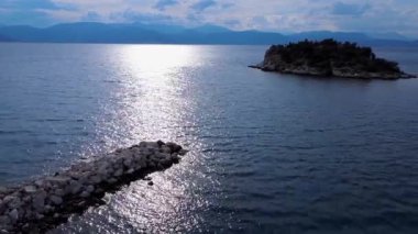 Yunanistan 'daki Ege Denizi üzerinde gün batımı sakin mavi sularda yumuşak altın bir ışık yaratıyor. Bu yaz Akdeniz manzarasında kayalık bir ada ve uzak dağlar belirir..