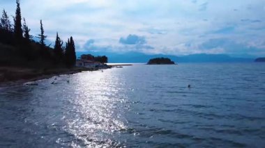 Bu drone görüntülerinde güneş battıktan hemen sonra bir Yunan adasında küçük doğal bir koy var. Arka planda küçük bir ada belirir ve sessiz kumsalı çevreleyen ağaçlar.