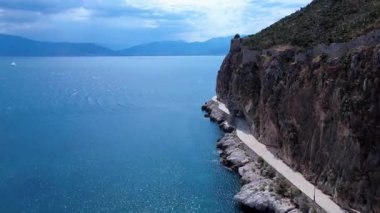 Bu Yunan videosunda sakin mavi denizin üzerinde dramatik bir uçurum var. Kayaların üzerinde kadim kale duvarları beliriyor yol sahil boyunca eserken.
