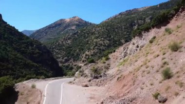 Yunanistan 'daki engebeli dağların üzerinden yükselen bir dron, dramatik bir geçitten geçen dolambaçlı bir yolu ortaya çıkarıyor. Akdeniz manzarası kayalık yamaçlarda sarp kayalıkları ve sık ağaçları gösteriyor..