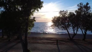 Deniz kenarındaki bir Yunan parkında, bir koşucu gün batımının altında hareket ederken, arabalar yakınlardan geçiyor ve Akdeniz 'deki doğa ile hareket arasındaki dengeyi yakalıyor..