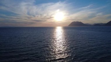 Yunanistan 'da Akdeniz ufkuna nefes kesici bir günbatımı yayılıyor. Denizde parlayan altın ışıkla ve uzaktaki yüksek dağ zirveleriyle..
