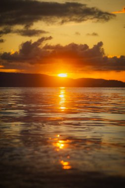 Gün batımında bir plaj sahnesi. Gün batımında güneş ışığı denize yansıyor. Aimoli Sahili, Alor, Doğu Nusa Tenggara - Endonezya
