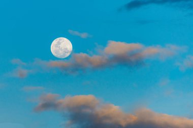 Alacakaranlıkta dolunay manzarası. Akşam gökyüzünde güzel bir ay. Mavi gökyüzünde, tüylü beyaz bulutlarla ay manzarası..