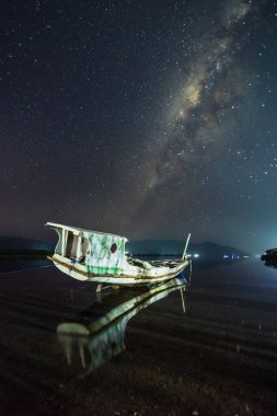 Samanyolu 'nun ortaya çıkmasıyla terk edilmiş bir teknenin gece yarısı görüntüsü. Alor, Doğu Nusa Tenggara - Endonezya