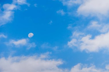 Öğleden sonra gökyüzünde güzel bir ay. Mavi gökyüzünde, tüylü beyaz bulutlarla ay manzarası..