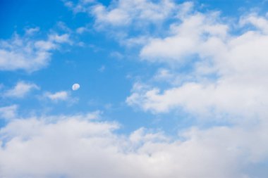 Öğleden sonra gökyüzünde güzel bir ay. Mavi gökyüzünde, tüylü beyaz bulutlarla ay manzarası..