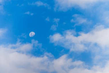 Öğleden sonra gökyüzünde güzel bir ay. Mavi gökyüzünde, tüylü beyaz bulutlarla ay manzarası..