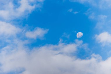 Öğleden sonra gökyüzünde güzel bir ay. Mavi gökyüzünde, tüylü beyaz bulutlarla ay manzarası..