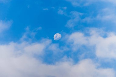 Öğleden sonra gökyüzünde güzel bir ay. Mavi gökyüzünde, tüylü beyaz bulutlarla ay manzarası..