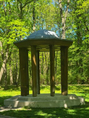 Yeşil yemyeşil bir ormanın ortasında kubbeli bir çatısı olan ahşap bir pavyon. Doğanın temaları, rahatlama, seyahat, parklar ve açık hava mimarisi için ideal bir bahar manzarası..