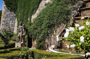 Bu yüksek çözünürlüklü fotoğraf halka açık bir parktaki dekoratif bir fıskiyenin serin bir görüntüsünü yakalıyor, yemyeşil bir zemin ve yumuşak bir akşam ışığı üzerine kurulmuş. Zarif mimari tasarımı ve kademeli akan suyuyla çeşme,