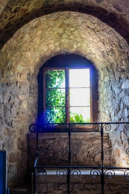 Bu yüksek kaliteli fotoğraf, geleneksel mimari ve doğal malzemelerin güzelliğini gösteren taştan bir duvara yerleştirilmiş büyüleyici bir pencere içeriyor. Taşların eskimiş dokusu, pencerenin eski ahşap çerçevesiyle birleşmiş.