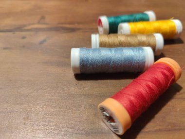 Ahşap bir yüzeye ustalıkla dizilmiş renkli dikiş ipliği makaralarının yakın çekim görüntüsü. Kırmızı, mavi, altın, yeşil ve kahverenginin canlı renkleri, el işi ve dikiş meraklıları için ideal görsel olarak memnun edici bir kompozisyon oluşturur..