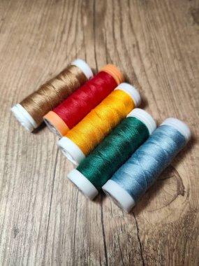 Kahverengi, kırmızı, sarı, yeşil ve mavi de dahil olmak üzere çeşitli renklerde dikiş ipliklerinden oluşan canlı bir düzenleme, kırsal ahşap arka plandaki el işi malzemelerinin güzelliğini gözler önüne seriyor..
