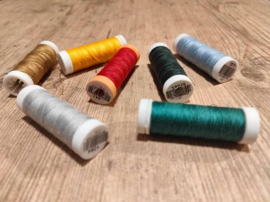 Ahşap bir yüzeye yayılmış çeşitli renkli dikiş ipliklerinden oluşan canlı bir düzenleme. Sahne, altın, sarı, kırmızı, yeşil, açık mavi, turuncu ve gümüş gibi neşeli renklerin bir karışımını yakalar. Çeşitlilik farklı dokuları vurgular