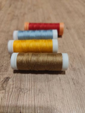 Kırsal ahşap bir masa üzerinde düzgün dizilmiş canlı dikiş ipliklerinin yakın plan görüntüsü. Kırmızı, altın, mavi ve sarı tonlarındaki iplikler görsel olarak çekici bir kompozisyon oluşturarak dikiş ve işçilikte ustalığı ve hassasiyeti vurguluyor. Şey... 