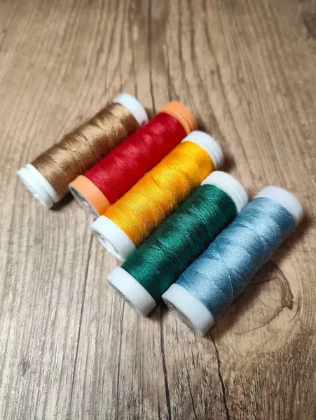 Kahverengi, kırmızı, sarı, yeşil ve mavi de dahil olmak üzere çeşitli renklerde dikiş ipliklerinden oluşan canlı bir düzenleme, kırsal ahşap arka plandaki el işi malzemelerinin güzelliğini gözler önüne seriyor..