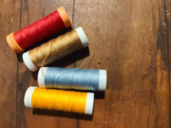 Kırsal ahşap bir yüzey üzerinde duran kırmızı, altın, mavi ve sarı da dahil olmak üzere dört iplik makarasından oluşan canlı bir görüntü. Ahşap zeminli ipliğin dokuları sıcak ve davetkar bir atmosfer yaratıyor.