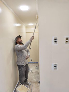 Bir marangozluk atölyesinin yakından görüntüsü, sarı matkaplar ve kulak koruyucular gibi güvenlik ekipmanları da dahil olmak üzere aletlerle dolu düzensiz bir çalışma tezgahını gösteriyor..