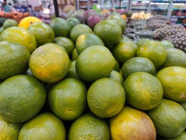 Bir markette bol miktarda taze yeşil limon yığını. Doğal ışık, canlı ve sulu meyveleri aydınlatıyor. Görüntü, yerel ürünleri takdir edenler için ideal bir tazelik ve sağlık hissi uyandırıyor..