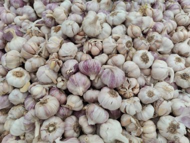 Mor, beyaz ve kremalı nüanslarını vurgulayan bir yığın taze sarımsak kafalar. Görüntü, sağlıklı gıda ve doğal mutfak bağlamında ideal bir pas ve tazelik hissi veriyor..