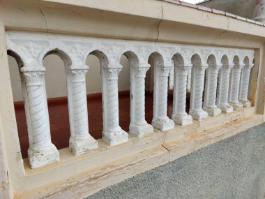 Neoklasik tarzda klasik sütunları olan bir balkon manzarası. Beyaz sütunlar, klasik mimari tasarımın tarihini ve sofistikesini vurgulayan hassas ayrıntılar ve görünür aşınmalar içeriyor..