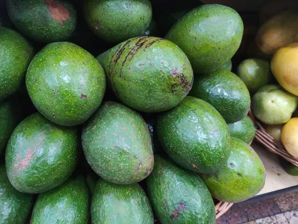 Bir pazar rafında parlak yeşil avokadolar bir araya getirilmiş. Canlı dokular ve renkler avokadoların tazeliğini ve kalitesini vurguluyor. Sağlıklı beslenme temaları için mükemmel..