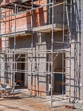 Görüntü, yapıyı destekleyen metal iskeleli yapıyı gösteriyor. Duvarlar tuğla ve harç gösteriyor. Organize yapı malzemeleriyle aktif bir çalışma ortamı.