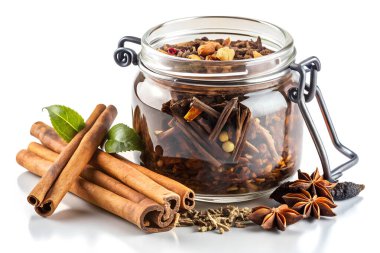 Tarçın çubukları, vanilya kabukları, yıldız anasonu ve yeşil yapraklarla çevrili bitki çayı yapraklarıyla dolu cam bir kavanoz görsel olarak çekici ve aromatik bir görüntü yaratıyor..