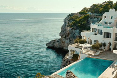 Bir Akdeniz uçurumuna tünemiş çarpıcı beyaz bir villa nefes kesici panoramik okyanus manzarası sunuyor. Geniş sonsuzluk havuzu masmavi denizle kusursuz bir şekilde harmanlanarak huzurlu ve lüks bir kaçış yaratıyor. Açık hava oturma alanları ve yemyeşil
