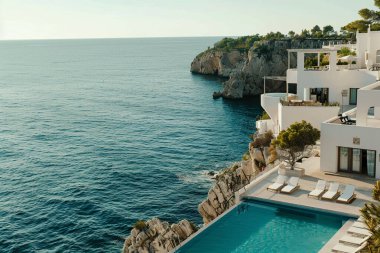 Büyüleyici beyaz bir villa, Akdeniz 'e bakan bir uçuruma çarpıcı bir şekilde tünemişti. Geniş sonsuzluk havuzu masmavi sularla kusursuz bir şekilde harmanlanarak nefes kesici bir manzara yaratır. Modern mimari engebeli kıyı manzarasını tamamlar.