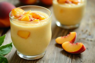 Meyve dilimleriyle süslenmiş, kırsal bir masaya konmuş şeftalili smoothie 'nin yakın plan görüntüsü. Smoothie ve şeftali parçalarını vurgular.