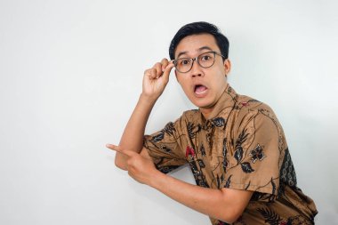 Pria asia yang ekspresif mengenakan batik dan kacamata dengan ekspresi çıktı, tangan menunjuk ke örnek Dan tangan lainya megang kacamata