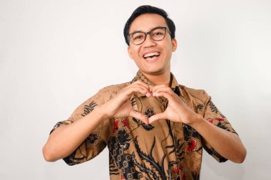 Batik takan, gülümseyen yüzlü gözlüklü, göğsünde aşk sembolü olan Asyalı bir adam.