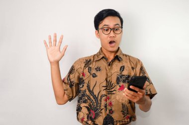Yüzünde batik gömlek ve gözlük olan Asyalı bir adam, bir elinde akıllı telefon, diğer elinde de yukarı doğru bakan bir el.