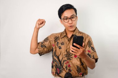 Akıllı telefona bakan Asyalı bir adam. Batik gömlek ve gözlük takıyor.