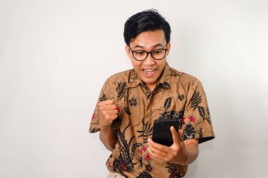 Mutlu yüzlü, batik gömlek ve gözlüklü Asyalı bir adam zaferi kutlamak için hareket ediyor.