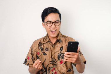 Gözlüklü Asyalı bir adam elinde akıllı bir telefonla zaferi mutlu bir ifadeyle kutluyor.