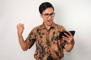 Mutlu yüzlü, gözlüklü, batik gömlekli, akıllı telefonuyla maçı izleyen Asyalı bir adam.