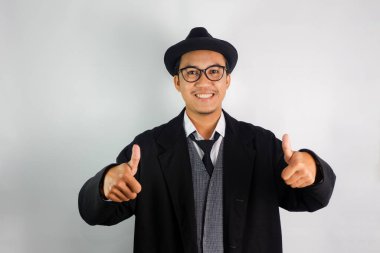 Asyalı bir adam mafya gibi giyinmiş, gözlük takıyor ve şapka takıyor. Dost canlısı bir yüzü var.