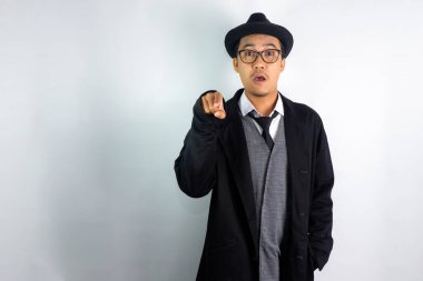 Mafya gibi giyinmiş, gözlüklü ve şapkalı bir Asyalı. Parmağı şaşkın bir ifadeyle öne doğru işaret ediyor.