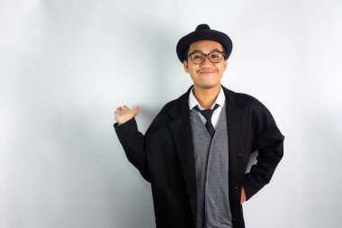 Mafya gibi giyinmiş, gözlüklü ve şapkalı Asyalı bir adam gülümseyen bir ifadeyle geriye doğru el hareketi yapıyor.