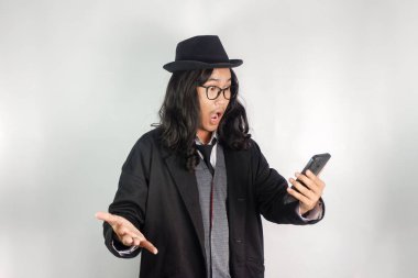 Uzun saçlı, mafya gibi giyinmiş, gözlüklü ve şapkalı bir Asyalı telefon görüşmesi yapıyor ve tuhaf hareketler yapıyor.